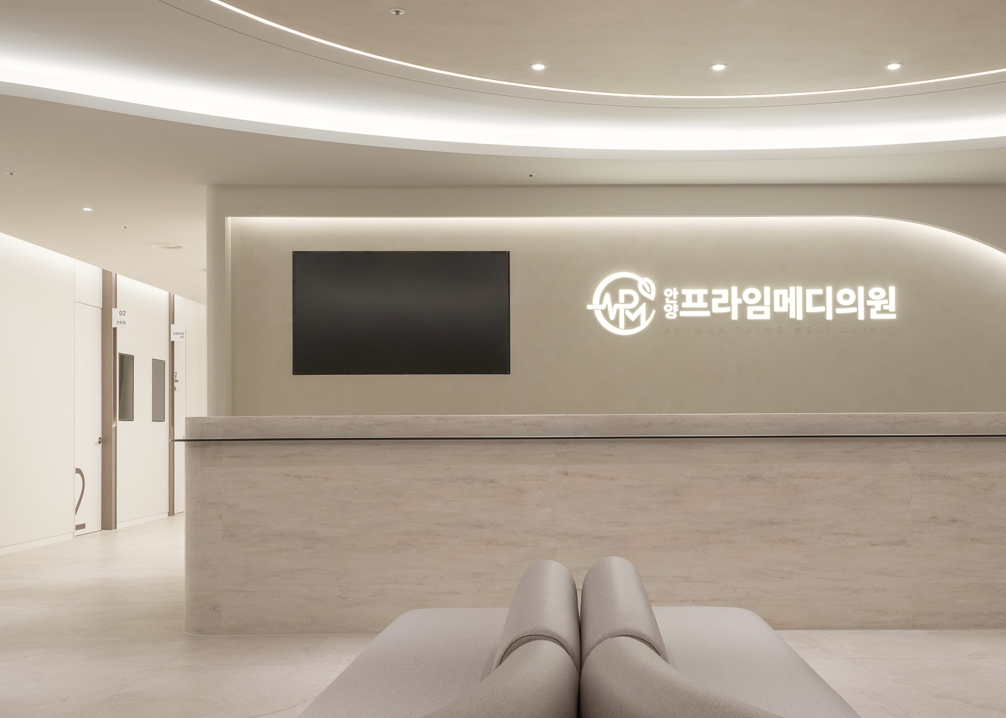 안양프라임메디의원 접수 공간. 병원 로고가 표시된 안내 모니터와 깔끔한 데스크가 배치되어 있어 정돈된 첫 방문 경험을 전달한다.