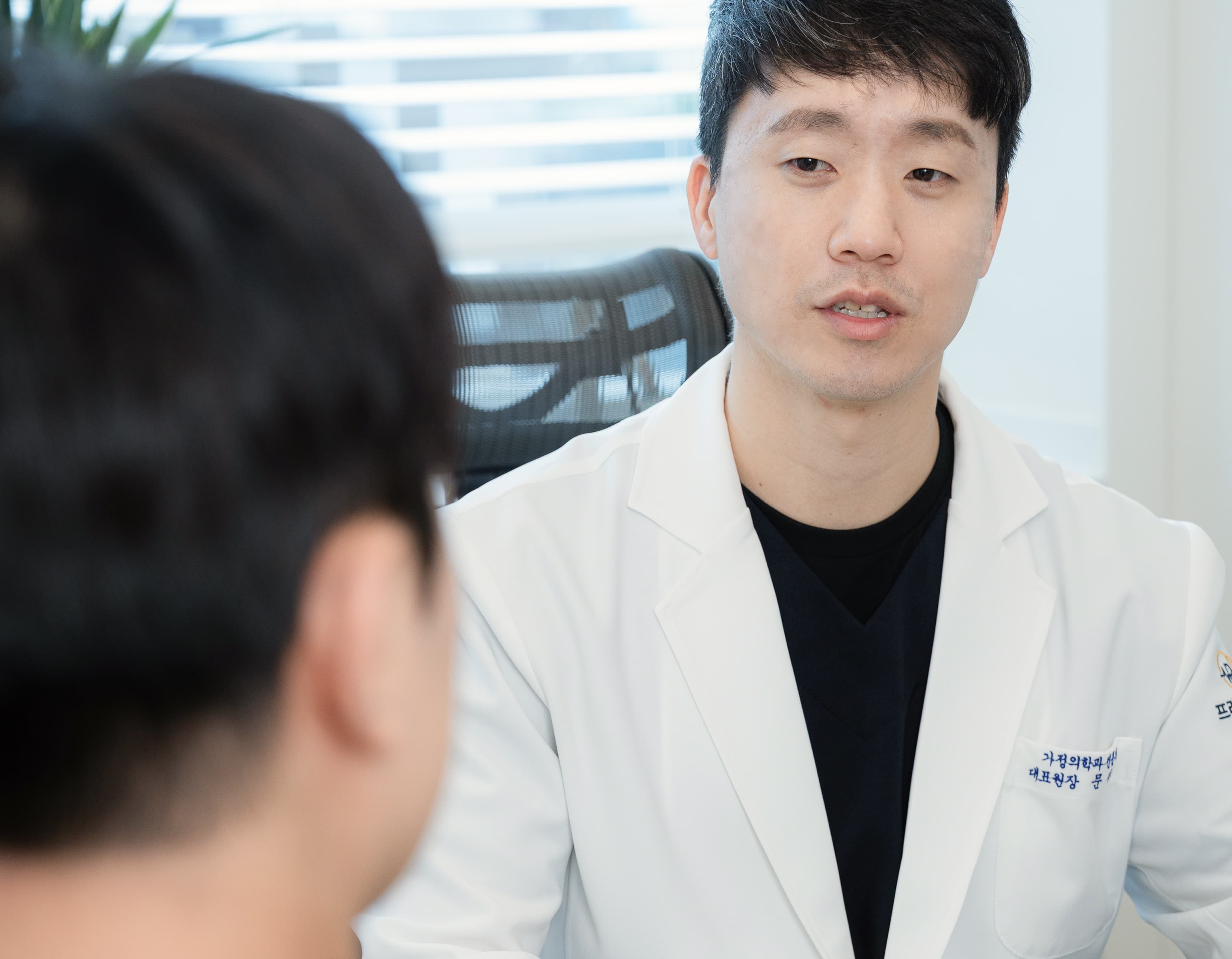 안양프라임메디의원 가정의학과 전문의 문다운 원장이 흰색 진료복을 입고 환자와 마주앉아 진료 상담을 진행하는 모습. 진지하고 신뢰감 있는 표정으로 환자의 이야기에 귀 기울이는 장면이 담겨 있다.