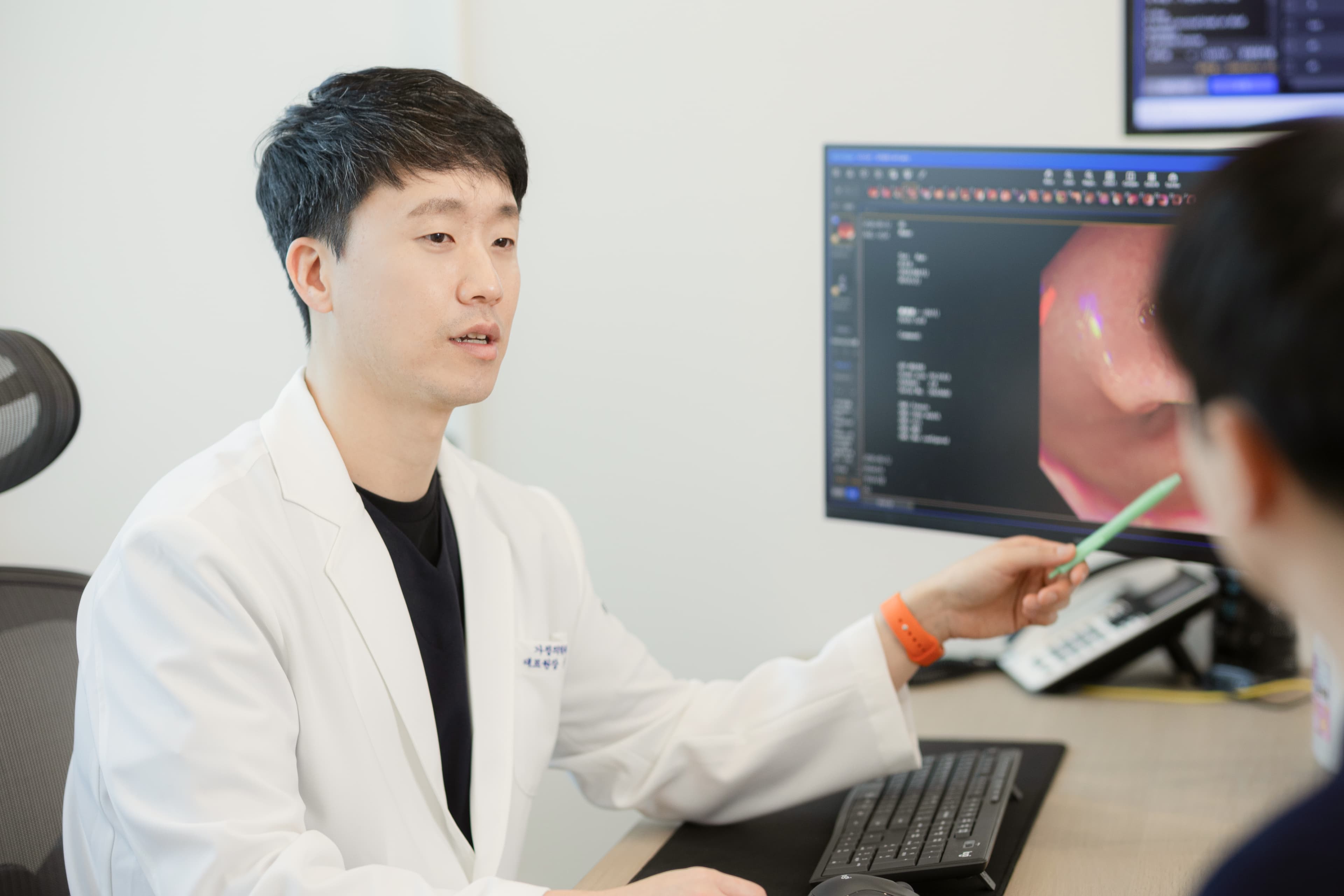 가정의학과 전문의 문다운 원장이 모니터 화면을 통해 검사 결과를 환자에게 설명하는 모습. 신뢰감 있는 태도로 진료 내용을 안내하는 장면이 담겨 있다.